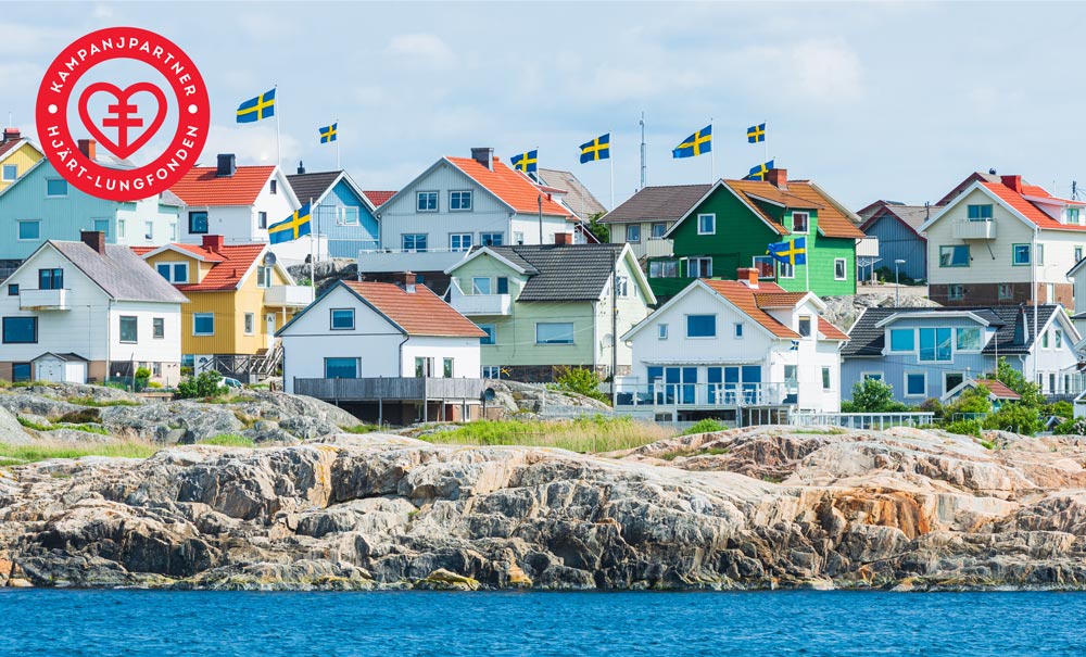 Skärgårdsvy med många hus precis vid vattnet i olika färger. I vänstra hörnet syns en logga i rött med texten Kampanjpartner Hjärt-lungfonden.